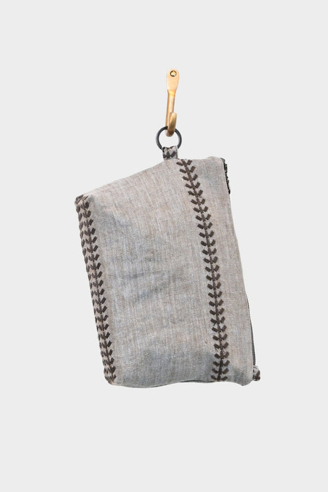 The Linen Trail- is a gray linen bag with decorative brown stitching, made from upcycled designer linen, shown folded and hanging from a brass hook against a plain white background.