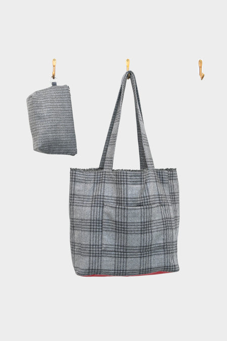 A grey wool plaid tote with a red leather base, from AVAILABLE AT PIERRE LAFOND, hangs on a central hook beside a matching folded accessory, both set against a plain white background.