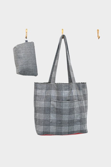 A grey wool plaid tote with a red leather base, from AVAILABLE AT PIERRE LAFOND, hangs on a central hook beside a matching folded accessory, both set against a plain white background.