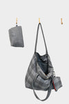 A gray AVAILABLE AT PIERRE LAFOND city flannel bag with a subtle checkered pattern hangs on a hook next to a matching folded pouch, both set against a plain white background.