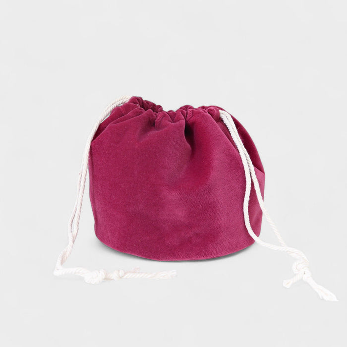 The Poppy Bag Fuchsia Velvet is a round velvet drawstring pouch with white cords, shown against a plain light gray background.