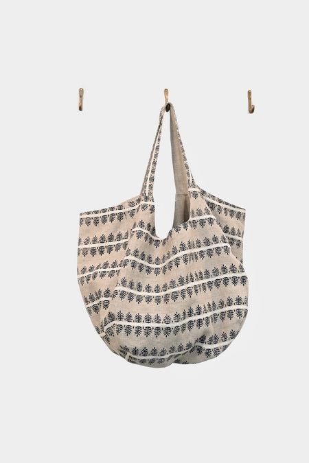 A large, beige Navy Fern tote from ABADIR, made of upcycled linen with navy leaf patterns, hangs from a center wall hook between two empty hooks on a plain white background. Contact ABADIR for details.