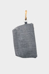 A gray textured fabric pouch with a herringbone pattern and red leather base hangs from a gold hook against a plain white background. Available at Pierre Lafond.