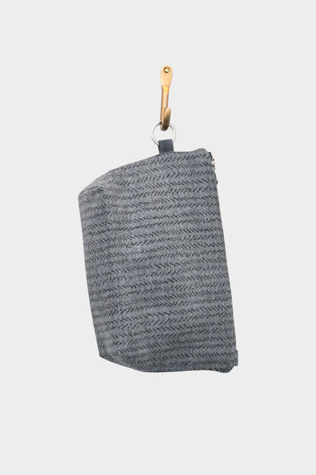 A Grey Flannel pouch—now available at Pierre Lafond—hangs from a tan leather hook, its subtle stitched pattern making it perfect for menswear accessories against a plain white background.