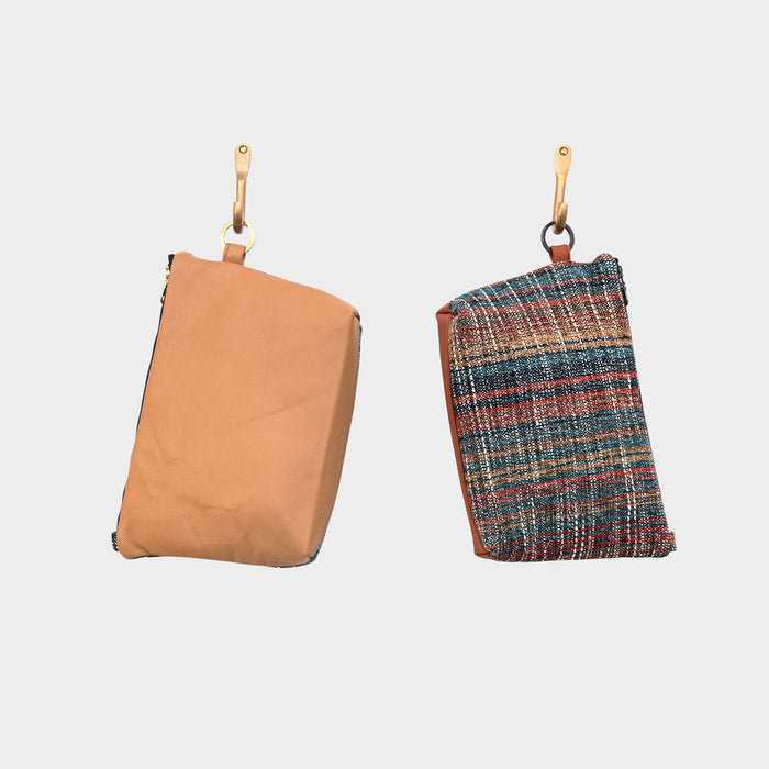 Two rectangular pouches hang from hooks: the left is a plain Camel Horizon mouse pouch in light brown, and the right is an upcycled leather pouch with a colorful woven front and brown leather sides. Both have gold hardware at the top.