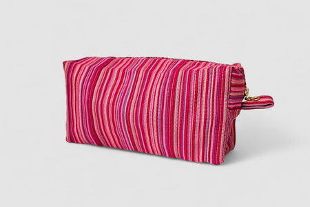 The SB Bag- Raspberry Stripe is a rectangular bag with pink, red, and purple vertical stripes on designer upholstery fabric. It has a gold zipper, small side handle, upcycled cotton lining, and is shown against a white background.
