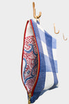 The Gingham Coast pouch, featuring blue and white gingham and a gold zipper, hangs on a wooden hook. Its partially open top reveals a white lining decorated with red and blue dots, set against a simple background.