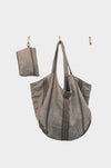 The Linen Trail- features a large gray artisanal handbag made from upcycled designer linen with dark stitched stripes, hanging alongside a matching small pouch on simple gold hooks against a plain white background.