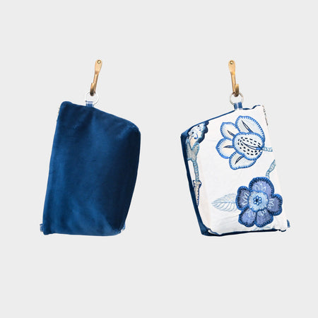Two Mini Mouse Pouch-Blue Garden hang by tan leather straps against a white background. The left pouch is royal blue velvet, and the right pouch features a white base with delicate blue floral embroidery.