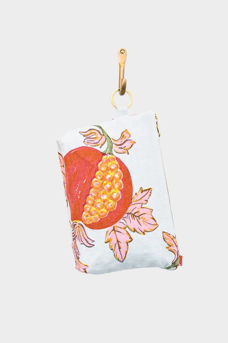 The Mightie Mouse Pouch- Pomegranate is a small designer zipper pouch with a gold zipper, tan leather loop, and a vibrant halved pomegranate and pink leaves design on a light blue background.