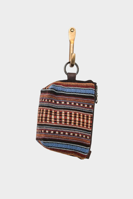 The Mini Mouse Pouch - Copper Canyon, a small rectangular woven pouch with colorful striped geometric patterns, hangs from a brass hook by a metal ring against a plain white background.