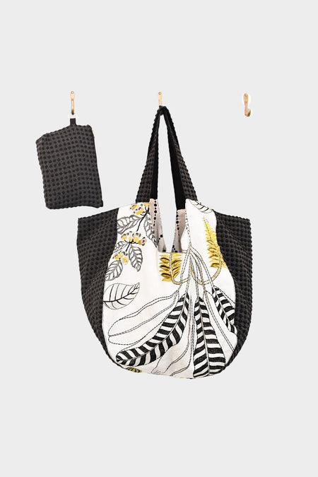 AVAILABLE AT PIERRE LAFOND: The reversible Bella Bag is a reusable shopping tote with black textured handles and sides, a white front with an embroidered botanical design, made from upcycled designer upholstery. Includes a matching small pouch.