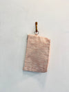 A folded Coral Stripe upcycled designer upholstery cloth in pink and white stripes hangs on a hook against a plain white wall.