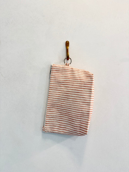 A folded Coral Stripe upcycled designer upholstery cloth in pink and white stripes hangs on a hook against a plain white wall.