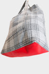 A close-up of a wool plaid tote with a bold red leather base, set against a white background. AVAILABLE AT PIERRE LAFOND.