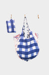 The Coastal Picnic tote—AVAILABLE AT ABADIR, contact for details—features a blue and white checkered design with partial red and white floral accents. It hangs on a hook beside its matching folded pouch. The bag is reversible.